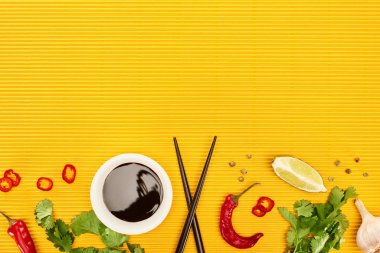 top view of fresh spices, vegetables, soy sauce and chopsticks on yellow surface