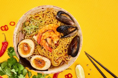 Taze malzemelerin yanında deniz mahsulleri ramen ve sarı yüzeyde yemek çubukları.