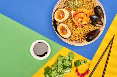 Taze malzemelerin yanında baharatlı deniz mahsulü ramen, kırmızı biber sosu ve rengarenk yemek çubukları.