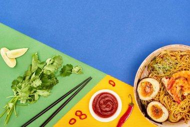 Taze malzemelerin yanında baharatlı deniz mahsulü ramen, kırmızı biber sosu ve rengarenk yemek çubukları.