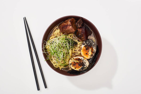 вид сверху на пряный мясной рамен возле палочек для еды на белой поверхности
