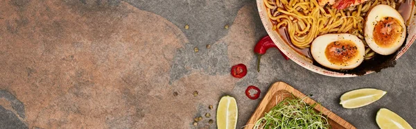 top view of spicy seafood ramen near fresh ingredients on stone surface, panoramic shot