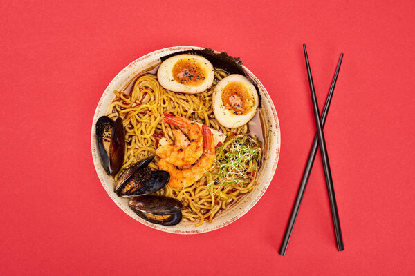 top view of spicy seafood ramen near chopsticks isolated on red