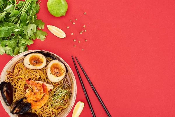 Top view of spicy seafood ramen near chopsticks, parsley and lime isolated on red — Stock Image Top View Spicy Seafood Ramen Chopsticks Parsley Lime Isolated Red Stock Photo