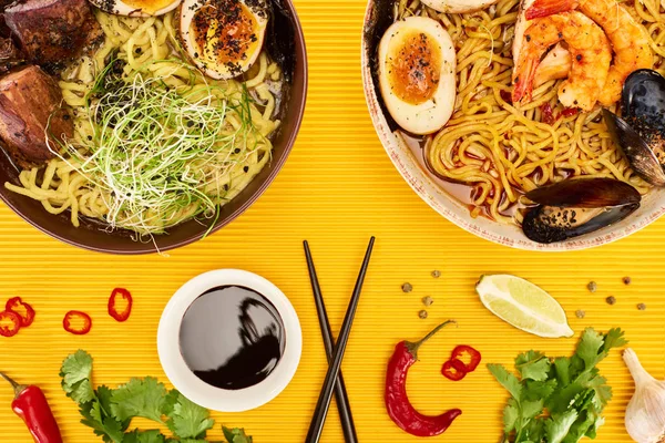 Top view of seafood and meat ramen near fresh ingredients, soy sauce and chopsticks on yellow surface — Stock Image Top View Seafood Meat Ramen Fresh Ingredients Soy Sauce Chopsticks Stock Picture