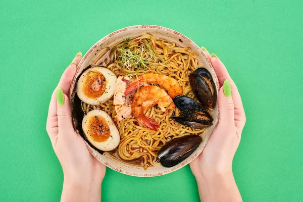 Cropped view of woman holding bowl with spicy seafood ramen on green surface — Stock Image Cropped View Woman Holding Bowl Spicy Seafood Ramen Green Surface Stock Photo
