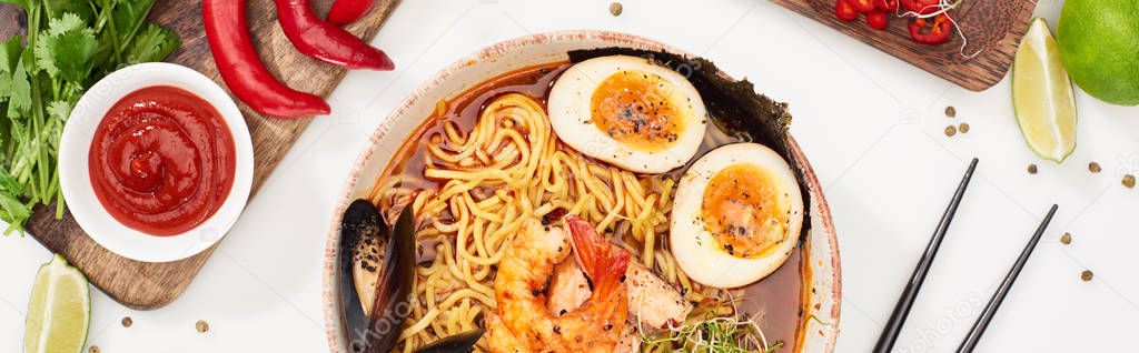 top view of spicy seafood ramen near fresh ingredients and chopsticks on white surface, panoramic shot