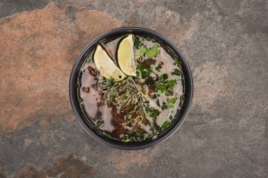 top view of pho in bowl with lime and coriander on stone background clipart