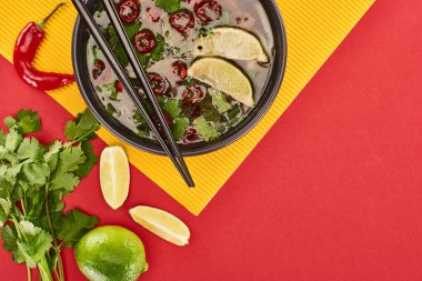 Limon, acı biber ve sarı arka planda kişniş ve yemek çubuklarıyla fotografın en üst görüntüsü.