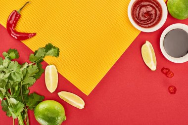 top view of lime, chili and soy sauces and coriander on red and yellow background clipart