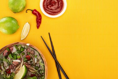 Çubukların yanındaki kasede pho 'nun üst görüntüsü, sarı dokulu arka planda limon, acı sos.