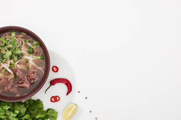 top view of pho in bowl near lime, chili and coriander on white background