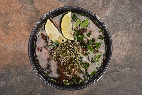 top view of pho in bowl with lime and coriander on stone background