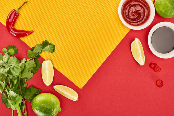 top view of lime, chili and soy sauces and coriander on red and yellow background