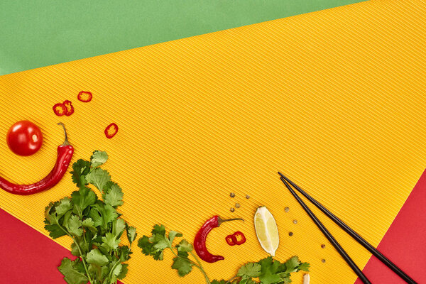 top view of chopsticks, lime, chili and coriander on red, green and yellow background