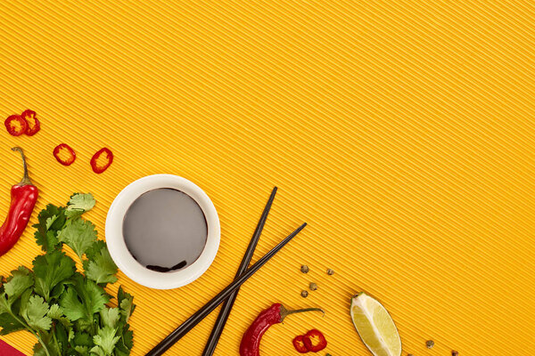 top view of chopsticks, lime, soy sauce and coriander on yellow background