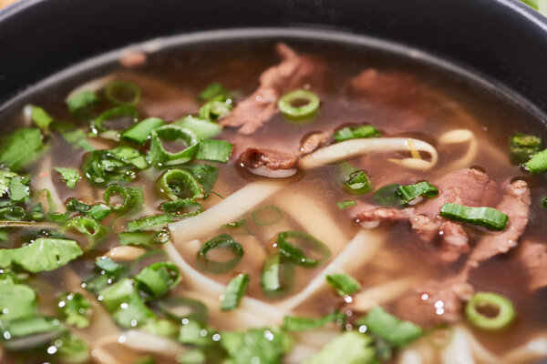 close up view of pho with noodles, meat, cilantro and green onion in bowl