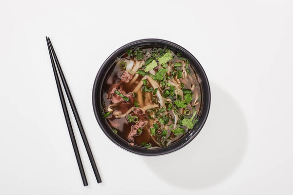 top view of pho in bowl near chopsticks on white background