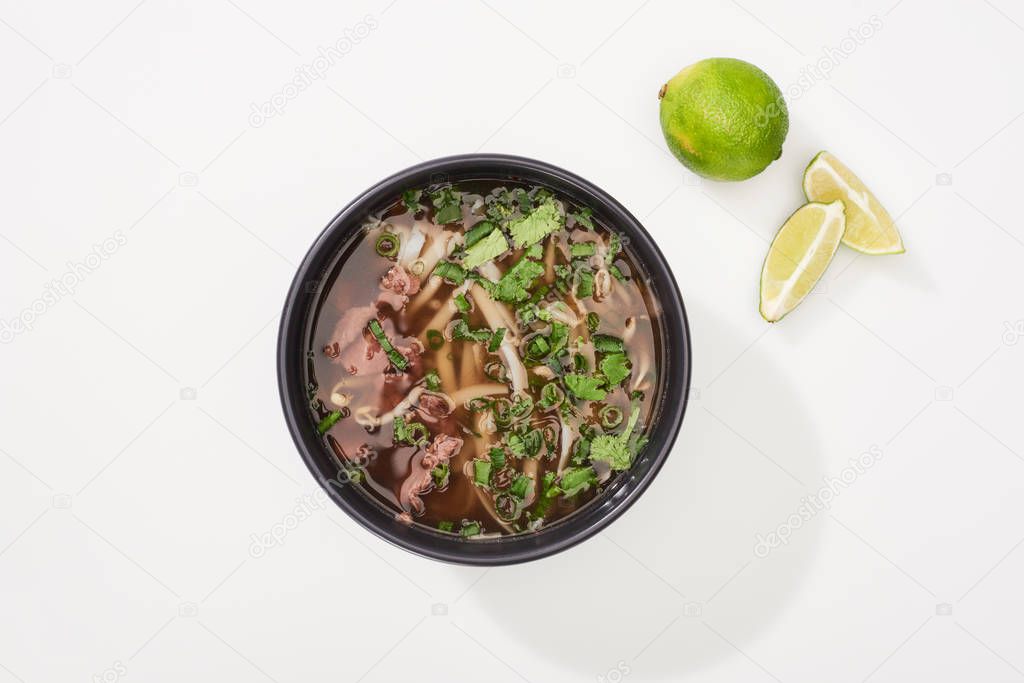 top view of pho in bowl near lime on white background