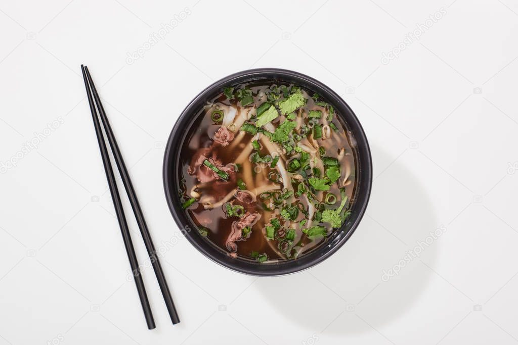 top view of pho in bowl near chopsticks on white background