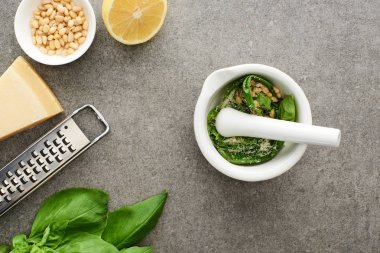 Pesto sosunun en üst görüntüsü ham malzemeler, rende ve pounder gri yüzeyde