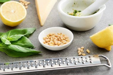 Gri yüzeyde pesto sosu, ham malzemeler ve pişirme aletlerinin görüntüsünü kapatın.