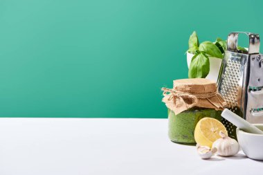 Kavanozda pesto sosu, malzemelerin yanında ve yeşil masada rende rende.