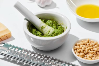 Pesto sosunun pounder 'ın içinde, rendeleyicinin yanında yakın görüntüsü, beyaz arka plandaki malzemeler.