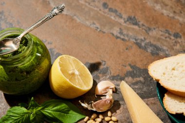 Baget dilimleri, kavanozda pesto sosu ve taş yüzeyinde taze malzemeler.