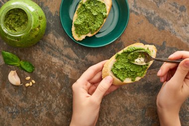 Kırpılmış bir kadın pesto sosu ve ekmek dilimlerini taş yüzeyine koyuyor.