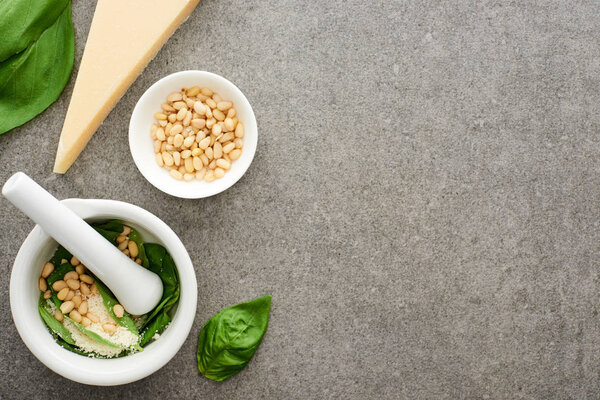 top view of pesto sauce raw ingredients and pounder on grey surface