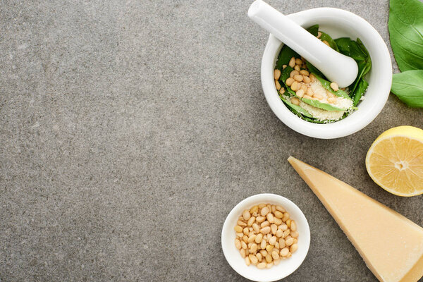 top view of pesto sauce raw ingredients and pounder on grey surface
