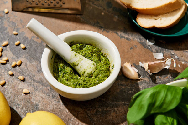 baguette slices, pesto sauce in pounder and fresh ingredients on stone surface