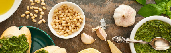 top view of baguette slices with pesto sauce on plate near fresh ingredients and cooking utensils on stone surface, panoramic shot