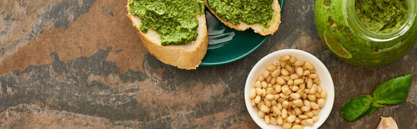 top view of baguette slices with pesto sauce on plate near fresh ingredients on stone surface, panoramic shot