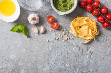 Domates, sarımsak, fesleğen, çam fıstığı, zeytinyağı, su ve pesto sosunun yanındaki çiğ Pappardelle 'in üst görüntüsü gri yüzeyde