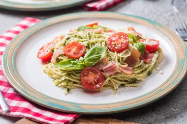 Gri yüzey üzerinde domatesli pappardelle, fesleğen ve prosciutto ve ekose peçete.