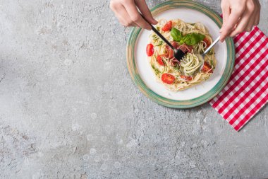 Gri yüzey üzerinde domatesli, fesleğenli ve jambonlu Pappardelle yiyen bir kadının kısmi görüntüsü