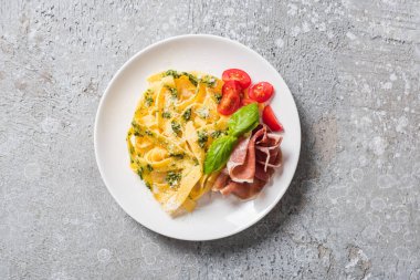 Domatesli pişmiş Pappardelle, pesto sosu ve gri yüzeyde prosciutto.