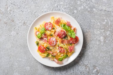 Domatesli pişmiş Pappardelle, pesto sosu ve gri yüzeyde prosciutto.