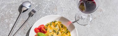 Gri yüzeyde kırmızı şarap ve çatal bıçak seti yanında domates, pesto ve prosciutto ile lezzetli Pappardelle manzarası, panoramik çekim