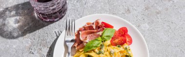 Domatesli, soslu, jambonlu, çatallı, gri yüzey kırmızı şaraplı, panoramik resimli Pappardelle 'in üst görüntüsü.