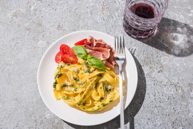 Lezzetli Pappardelle 'in üst görüntüsü domatesli, soslu ve çatallı jambonlu gri yüzeye yakın kırmızı şarap.