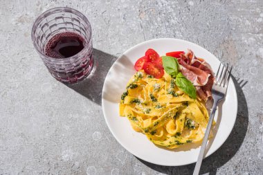 Lezzetli Pappardelle 'in üst görüntüsü domatesli, soslu ve çatallı jambonlu gri yüzeye yakın kırmızı şarap.