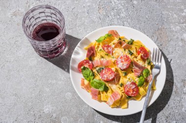 Lezzetli Pappardelle 'in üst görüntüsü domatesli, soslu ve çatallı jambonlu gri yüzeye yakın kırmızı şarap.