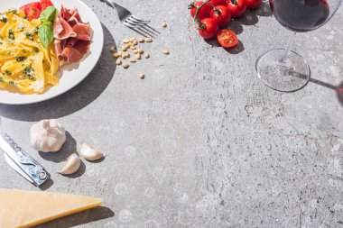 Taze domatesli Pappardelle, pesto ve prosciutto yanında kırmızı şarap ve gri yüzeydeki malzemeler.