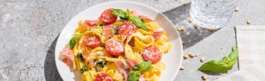 Suyun yanında domates, pesto ve prosciutto, gri yüzeyde peçete ve çam fıstığı, panoramik çekim