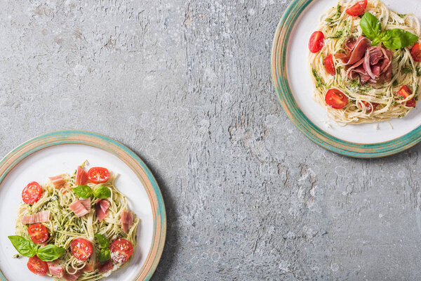 top view of Pappardelle with tomatoes, basil and prosciutto on plates on grey surface