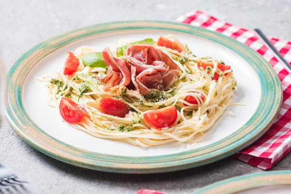 Pappardelle with tomatoes, basil and prosciutto on grey surface with plaid napkin