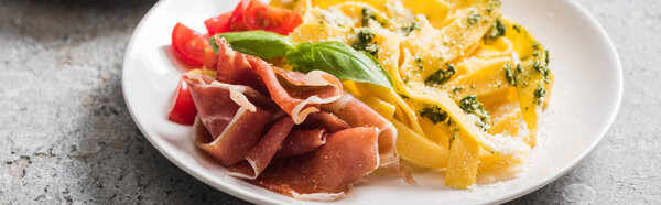 delicious Pappardelle with tomatoes, basil and prosciutto on grey surface, panoramic shot